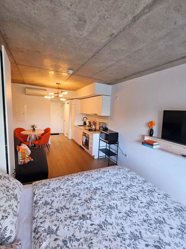 Un apartamento moderno con kitchenette, zona de comedor y sala de estar con sofá y televisor.