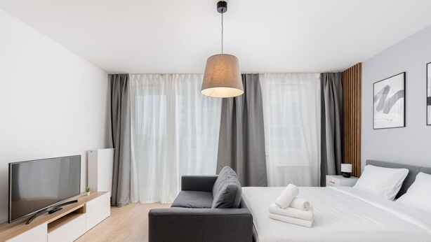 Ein modernes Hotelzimmer mit Flachbildfernseher, einer Couch, einem Bett mit weißen Bettwäsche und einer Pendelleuchte.