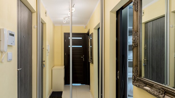 Un pasillo con una puerta de cristal que da a una habitación, un espejo con un marco decorativo y un teléfono en la pared.