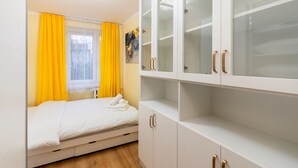 Un dormitorio con cama, armario de puertas de cristal y ventana con cortinas amarillas.