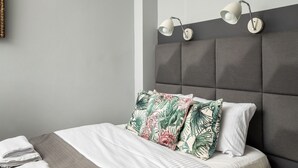 A neatly made bed with a grey headboard, two wall-mounted lamps, and tropical-patterned pillows. - Old Town Colourful Apartment (Warszawa)