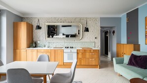A modern kitchen with wooden cabinets, a white countertop, and a built-in oven. There is a dining table with chairs and a light-colored rug. - Old Town Colourful Apartment (Warszawa)