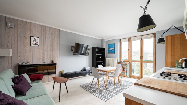 A modern living room with a sofa, dining table, and chairs, a kitchen area with a stove, and a TV mounted on the wall. - Old Town Colourful Apartment (Warszawa)
