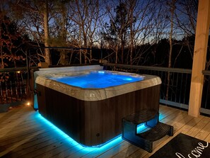 Ein Whirlpool auf einer Holzterrasse mit Geländer, umgeben von Bäumen.