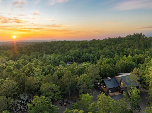 Ein modernes Haus, umgeben von dichtem Wald, mit freiem Blick auf den Sonnenuntergang.