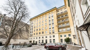 A multi-story building with balconies, parked cars, and a snow-covered ground.