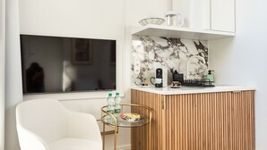 A modern kitchen with a wooden countertop, a white chair, a small round table with bottles, and a clock on the wall.