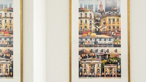 A wall with multiple framed artworks depicting urban scenes.