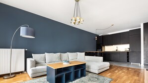 Una sala de estar moderna con un sofá gris, una mesa de centro de madera y una alfombra azul. Se ve un área de cocina al fondo.