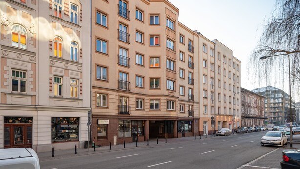 A multi-story hotel with a classic architectural style, featuring a central entrance with a canopy, multiple balconies, and a street view with parked cars. - Park Praski 2-Bedroom Apartment (Warszawa)