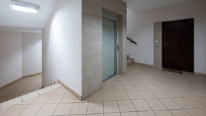 A hallway with a tiled floor, a door with a glass panel, and a staircase leading to an upper level. - Park Praski 2-Bedroom Apartment (Warszawa)