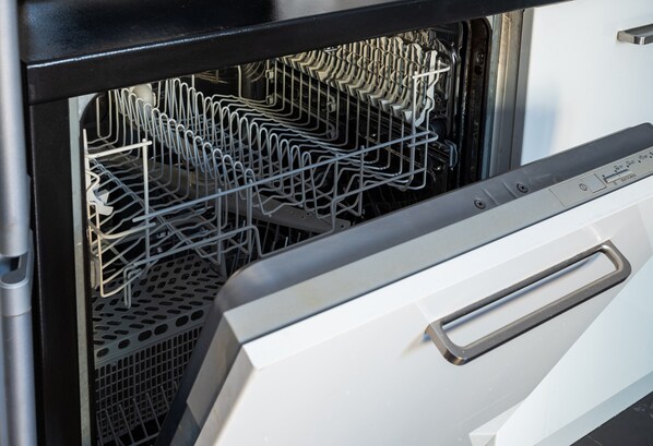 An open dishwasher with racks of dishes inside.