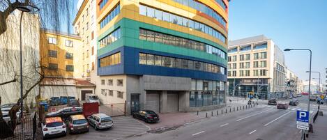 A multi-story building with a curved facade, parked cars along the street, and a clear blue sky.