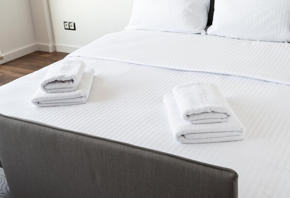 A neatly made bed with white linens and two folded towels on the headboard.