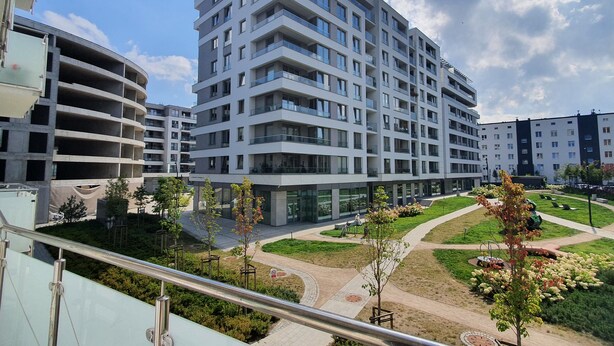 En modern byggnad med flera våningar, balkonger, en vackert anlagd innergård och en gångväg för fotgängare.