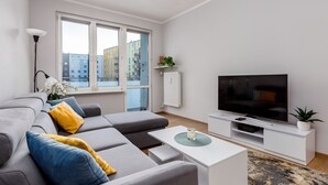 Ett modernt vardagsrum med en grå soffa, en platt-TV och ett vitt soffbord.