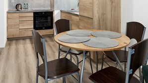 A modern kitchen with grey cabinets, a wooden dining table with four chairs, and a large wooden accent wall. - Poznań Airport Comfy Apartment (Poznań)