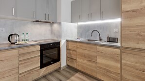 A modern kitchen with grey cabinets, wooden lower cabinets, a built-in oven, and a stainless steel sink. - Poznań Airport Comfy Apartment (Poznań)