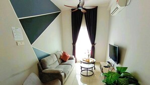 Un salon avec un canapé, un fauteuil, une table basse, un téléviseur et une plante.