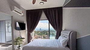 Une chambre moderne avec un grand lit, un ventilateur de plafond, une télévision et une vue sur la ville grâce à de grandes fenêtres.