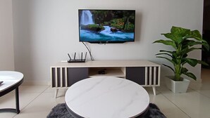 Un salon moderne avec un téléviseur à écran plat fixé au mur, une table basse ronde, un canapé blanc, une petite table blanche et une plante en pot.