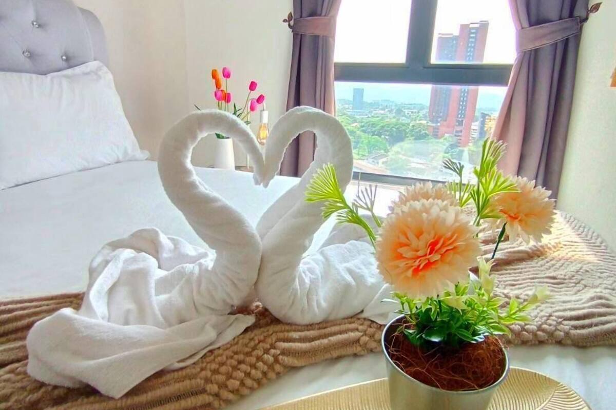 Een hotelkamer met een bed, een raam met gordijnen, een dienblad met handdoeken, een bloemstuk en een kleine kamerplant.