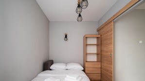 A bedroom with a bed, a wooden wardrobe, a wall-mounted light, and a ceiling light fixture. - Bemowo Lazurowa Chic Apartment (Warszawa)