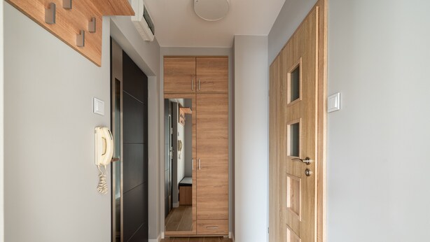 A hallway with wooden cabinets, a telephone, and a bench. - Bemowo Lazurowa Chic Apartment (Warszawa)