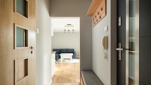 A hallway with a wooden door, a bench, and a view into a living room with a blue sofa and a white coffee table. - Bemowo Lazurowa Chic Apartment (Warszawa)