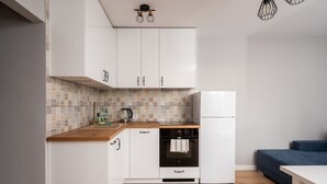 A compact kitchen with white cabinets, a wooden countertop, a patterned backsplash, and a built-in oven. - Bemowo Lazurowa Chic Apartment (Warszawa)