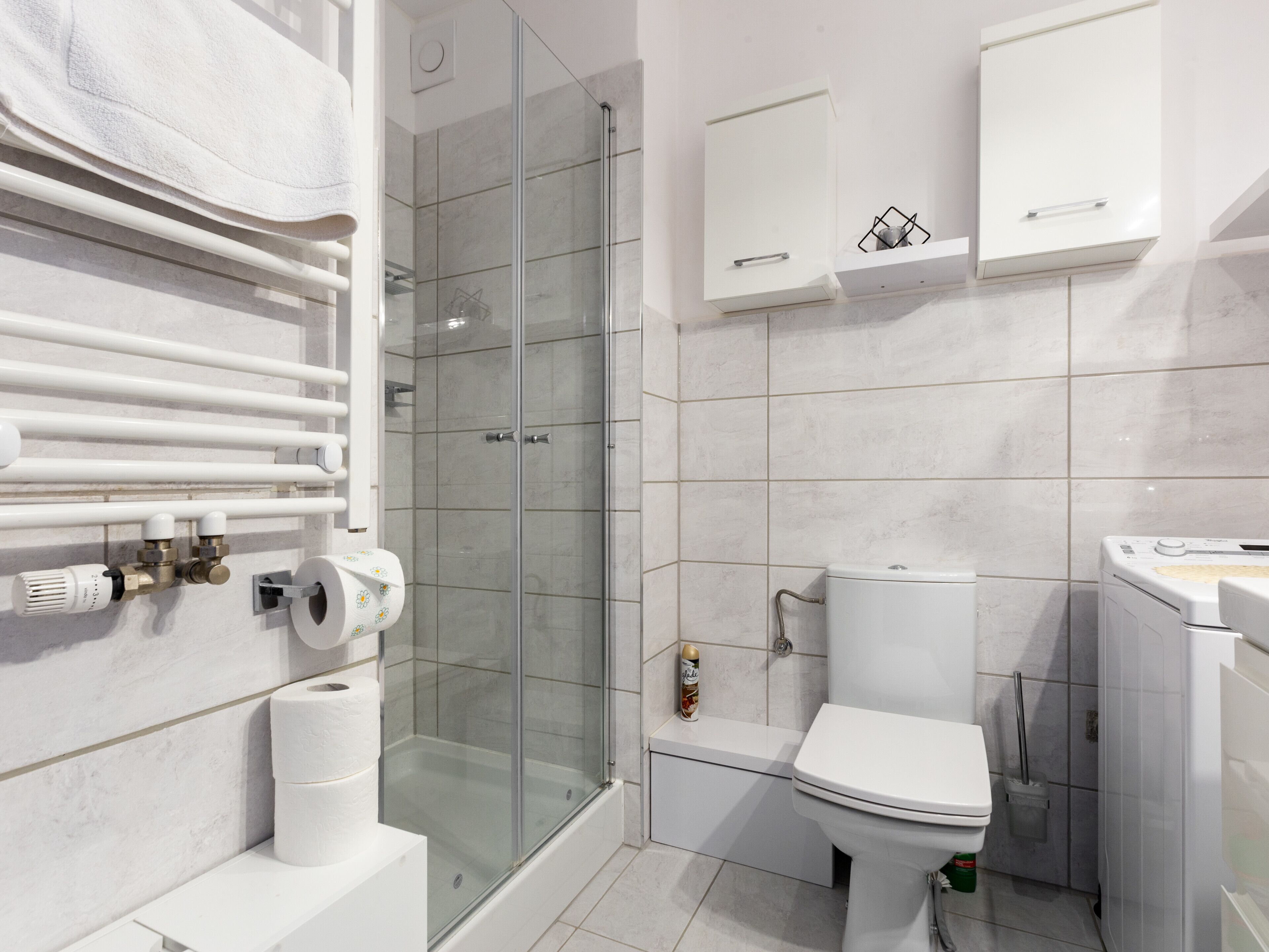 Une salle de bain moderne dotée d’une douche à parois de verre, de toilettes et d’un lave-linge.
