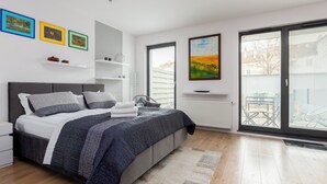 Ein modernes Schlafzimmer mit Bett, Nachttischen, Heizkörper und großen Fenstern mit Jalousien.