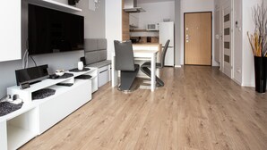 Ein modernes Wohnzimmer mit Flachbildfernseher, einer Couch, einem Esstisch mit Stühlen und einer Küchenzeile inklusive Mikrowelle und Kühlschrank.
