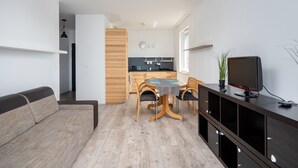 Un salon moderne avec un canapé, une table à manger et des chaises, un téléviseur, et un coin cuisine à l’arrière-plan.