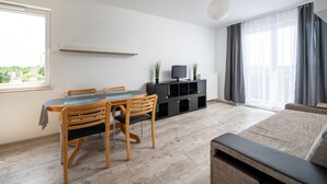 Un salon moderne comprenant un coin repas, un téléviseur à écran plat posé sur un meuble noir et une grande fenêtre agrémentée de rideaux.