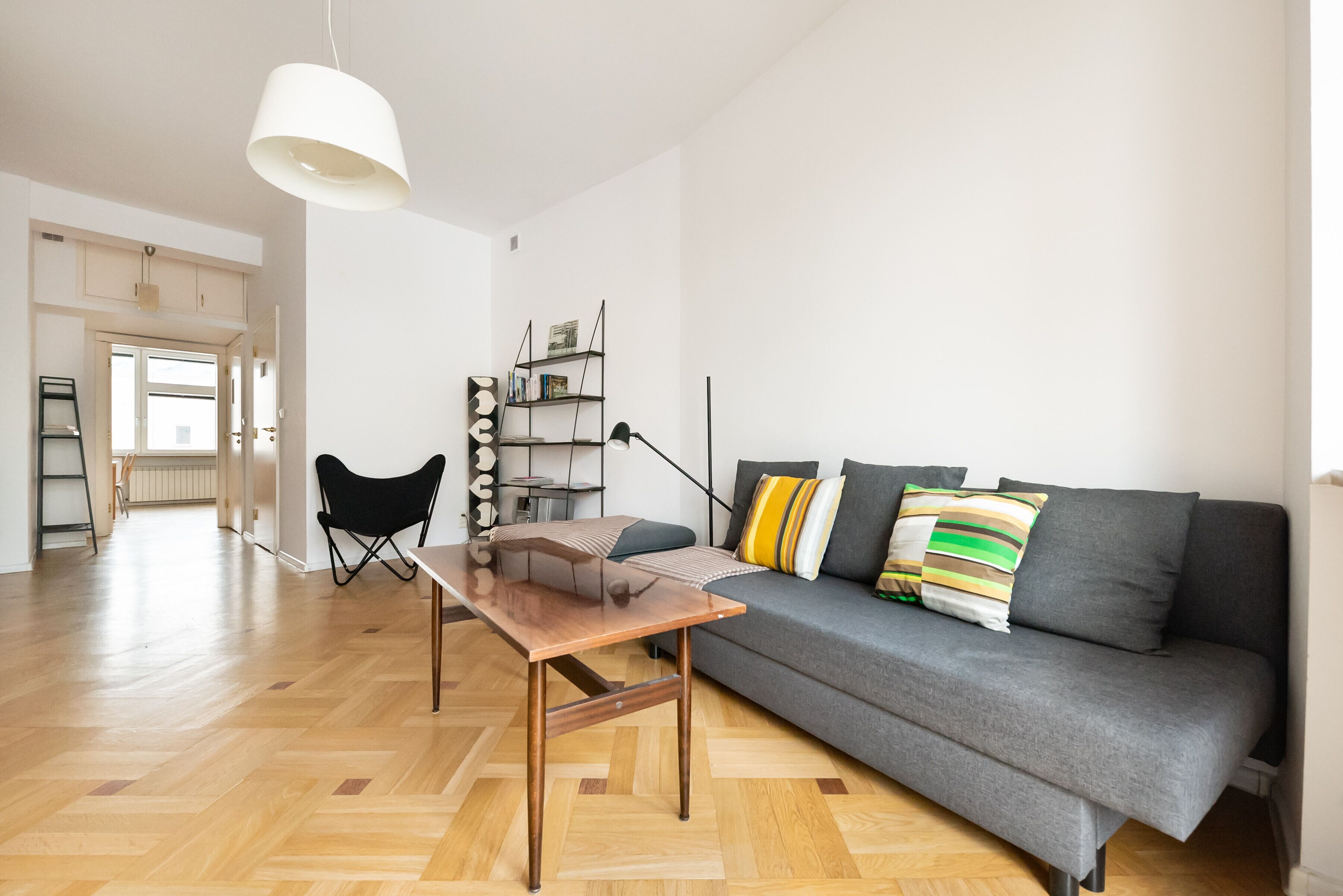 Un salon moderne avec un canapé gris, une table basse en bois et une chaise pliante noire.