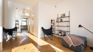 Ein modernes Wohnzimmer mit einer Couch, einem schwarzen Sessel, einem Bücherregal und einer Lampe.