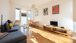 Ein modernes Wohnzimmer mit einer Couch, einem Esstisch, Stühlen, einem Fernseher und Kunstwerken an den Wänden.