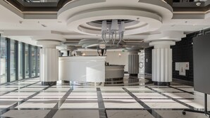 A modern lobby with a marble floor, a reception desk, and a large chandelier.