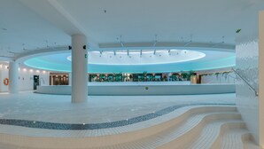 A spacious atrium with a central circular seating area, a tiled floor, and a modern ceiling design.