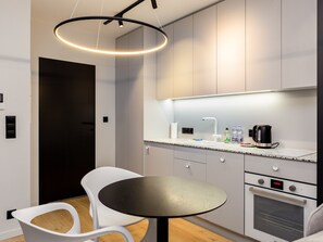 A modern kitchen with a round table, white chairs, a built-in oven, and a coffee maker.