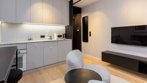 A modern kitchen with grey cabinets, a built-in oven, and a dining area with a table and chairs. - Quercus Deluxe Studio #B (Gdansk)