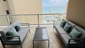 A balcony with two grey sofas, a glass coffee table, and patterned cushions. The balcony has a view of a beach and a pool area. - Beautiful 3 bedroom/3 bathroom Condo In Las Palomas Beach & Golf Resort (Puerto Penasco)