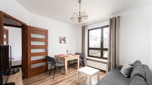 En moderne stue med en grå sofa, et træspisebord med stole, et hvidt sofabord og et stort vindue med gardiner.