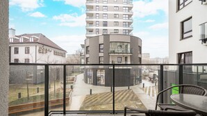 En balkon med udsigt over en moderne bygning, en belagt plads og et par stole.