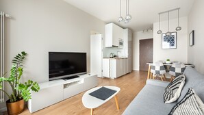 Un salon moderne avec un téléviseur à écran plat, un canapé blanc, une petite table et un coin repas avec une nappe à carreaux.