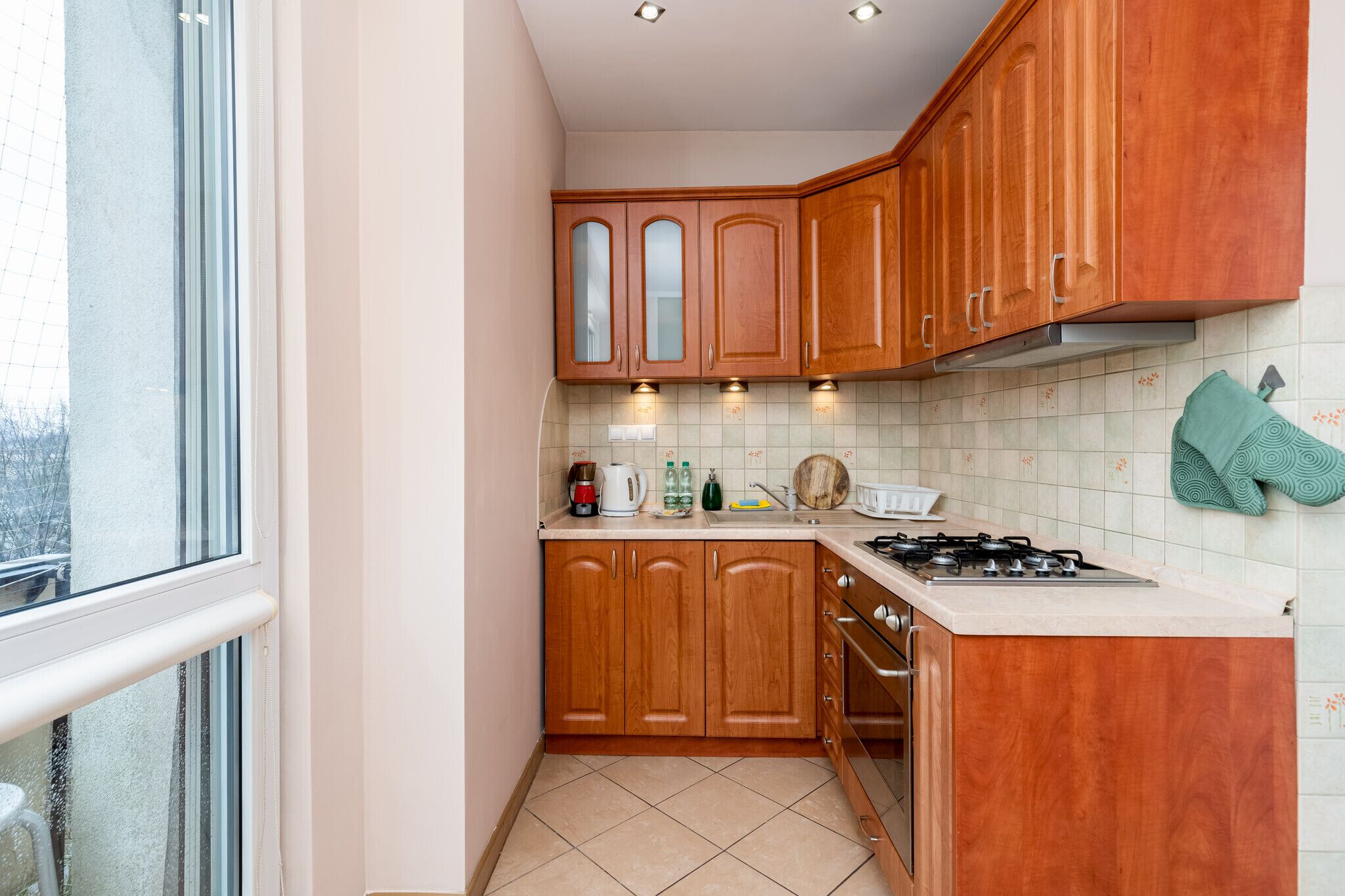Cocina compacta con armarios de madera, cocina a gas y ventana con vistas a un balcón.