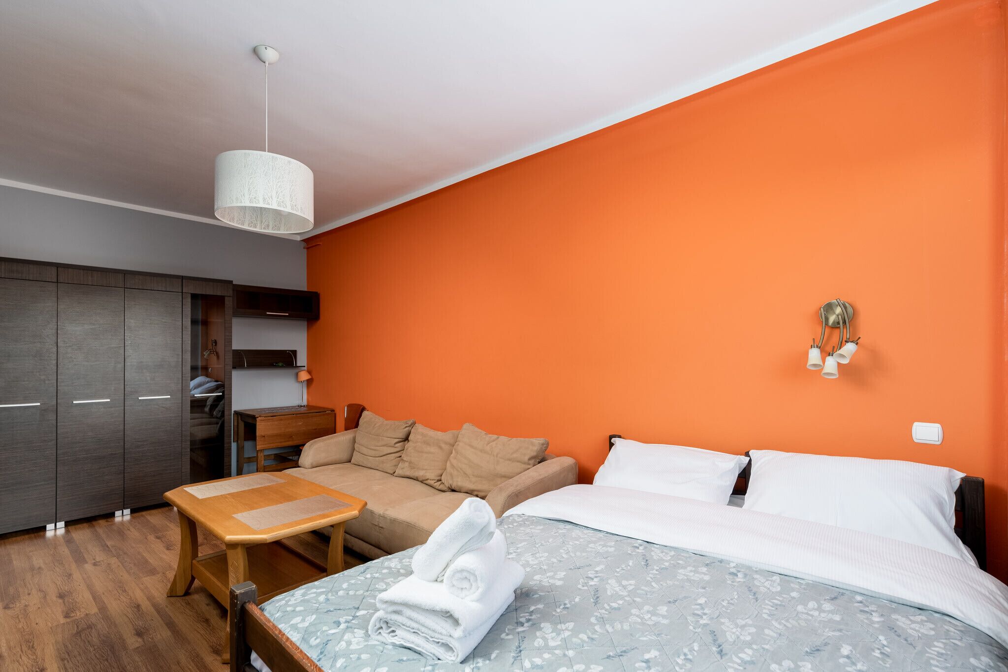 A hotel room with a bed, a sofa, a wooden table, and a wardrobe.