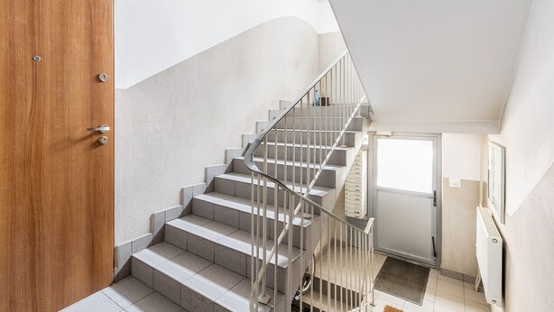 A modern staircase with a wooden door at the bottom and a metal railing. - Krowoderskich Zuchów Standard Studio (Kraków)