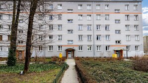 A multi-story residential building with a central entrance, a paved pathway leading to the entrance, and a small garden area with trees and shrubs. - Krowoderskich Zuchów Standard Studio (Kraków)